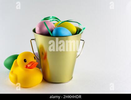 Rubber duck and a pail of pastel Easter eggs on a white background with copy space. Stock Photo