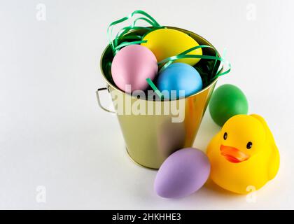 Rubber duck and a pail of pastel Easter eggs on a white background with copy space. Stock Photo