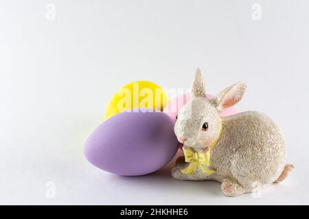 Easter bunny figurine with three Easter eggs on white background with copy space. Stock Photo