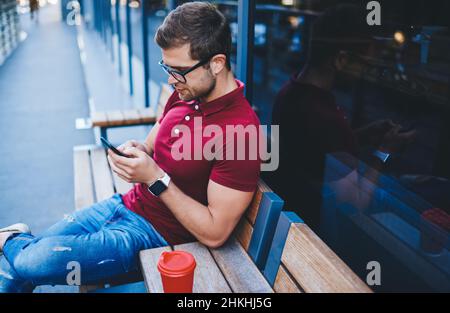 Serious young guy resting on bench while surfing cellphone Stock Photo