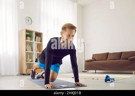 Portrait of happy athletic man who uses wireless headphones while doing sports at home. Stock Photo