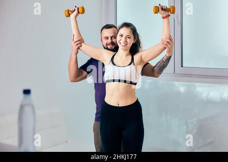 Fitness at home by woman with husband-trainer using dumbbells. Stock Photo