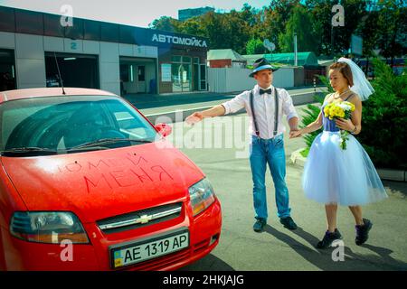 Dnepropetrovsk, Ukraine - 09.11.2016: A young man in a hat and a woman with a bouquet of flowers near the car. On the hood in Russian is written 'wash Stock Photo