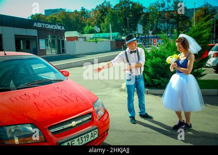 Dnepropetrovsk, Ukraine - 09.11.2016: A young man in a hat and a woman with a bouquet of flowers near the car. On the hood in Russian is written 'wash Stock Photo