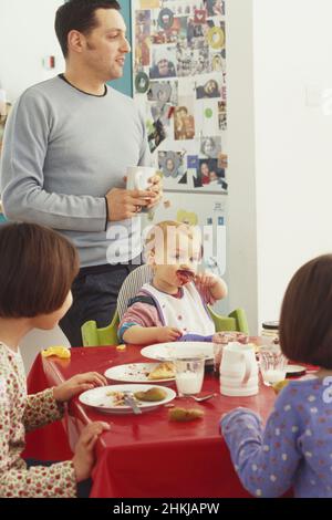 Toddler sitting in highchair at table eating off spoon Stock Photo