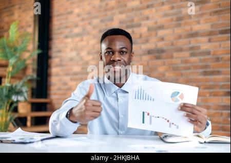 African american successful attractive young man, manager or financial consultant, communicates with partners by video call, presents a graph, discusses strategy, remote negotiations,shows a thumbs up Stock Photo