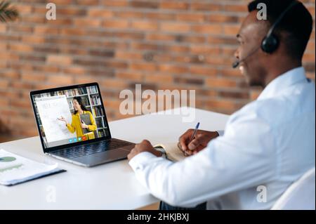 E-learning. Successful smart young african american man, looking at laptop screen, listening online lecture by video conference, taking notes during virtual webinar, brainstorming, improving skills Stock Photo
