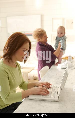 Mother using laptop as grandmother holds grandson Stock Photo