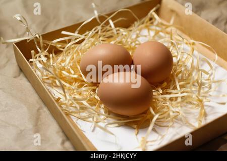 Closeup rustic eggs in box on craft background. Easter craft box with brown eggs on eco background. Chicken eggs on craft table with hay and straw. Cl Stock Photo