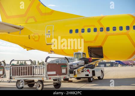 Yellow passenger aircraft and baggage cart with travel bags at airfield Stock Photo