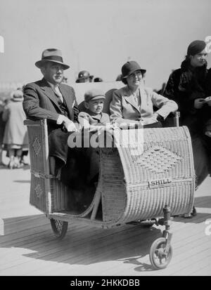A family is shown in a Shill Co. wicker rolling car on the Atlantic City boardwalk, ca. 1935. Stock Photo