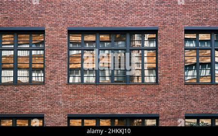 Facade wall of a brick building with windows. The opposite wall reflected in the window pane. Smooth rows of old masonry. Background image, screensave Stock Photo