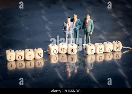 Miniature model of businessmen and wooden cubes with join our team inscription strung on a thread on reflective table. The recruitment business concep Stock Photo