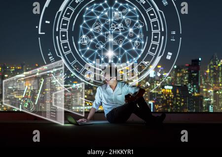 Asian businessman sitting and using the laptop and working with brain and virtual screen connecting with cloud technology over the cityscape backgroun Stock Photo