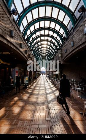 A Japanese male office worker or salaryman walks through an arched shopping arcade.near Iidabashi, Tokyo, Japan. Stock Photo