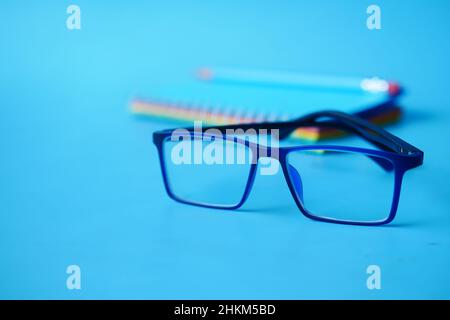 notepad, eyeglass and a pencil on blue background  Stock Photo