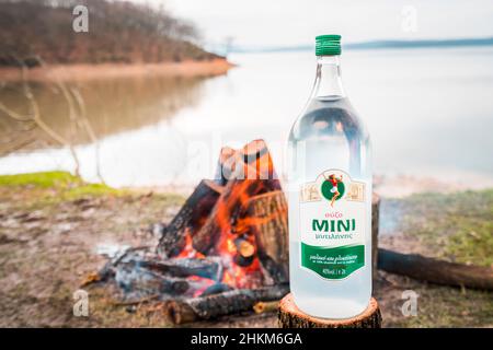 Bottle of Greek anise alcoholic beverage Ouzo on tree stump with camp fire in the background. Stock Photo