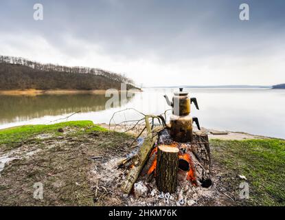 Turkish traditional teapot boiling on campfire, a smooth lake in the background. Stock Photo