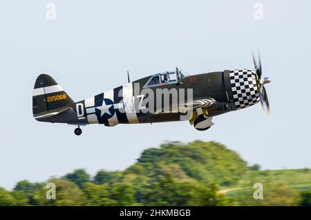 Republic P-47 Thunderbolt Second World War fighter plane in olive drab with invasion stripes and checkerboard nose cowling taking off at an airshow Stock Photo