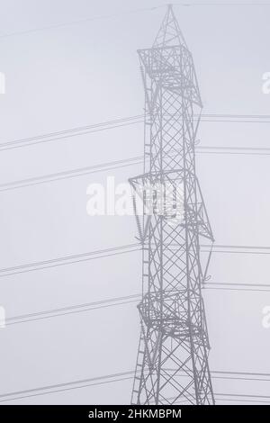 A large high-voltage pylon is shrouded in the morning mist Stock Photo