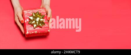 Women's hands with red manicure holds a gift box on a red background with space for text. Stock Photo