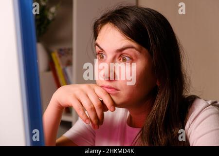 The woman raised her eyebrows up looking surprised at the computer screen, reading the news Stock Photo