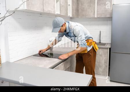 Master installs electric hob on kitchen cabinet. Stock Photo