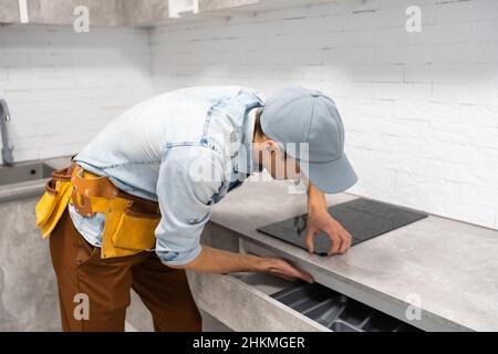 Master installs electric hob on kitchen cabinet. Stock Photo