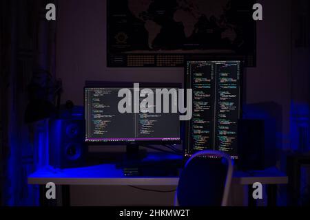 A man sits at a computer in a room at a table at night with blue lighting and programs Stock Photo