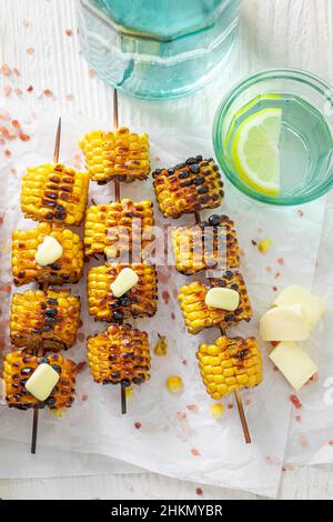 Sweet grilled corn cob with melting butter on stick. Corn grilled with butter on bonfire. Stock Photo