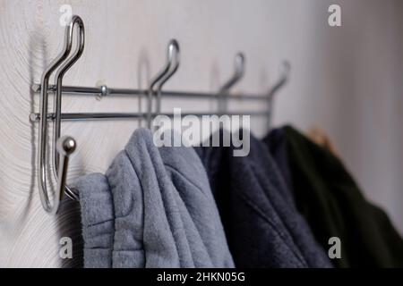Extremely close up various clothes hang on metal wall hanger, hooks with clothes hangers on white wall, selective focus Stock Photo