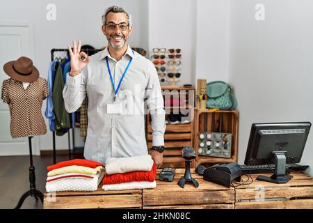 Middle age hispanic man working as manager at retail boutique smiling positive doing ok sign with hand and fingers. successful expression. Stock Photo