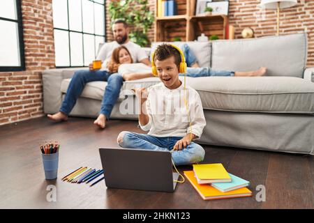 Family of three doing homework at home pointing thumb up to the side smiling happy with open mouth Stock Photo