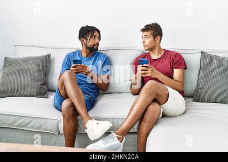 Two men friends using smartphone sitting on sofa at home Stock Photo
