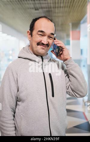 Portrait of senior asian man in grey hoodie talking mobile phone and smiling. Stock Photo