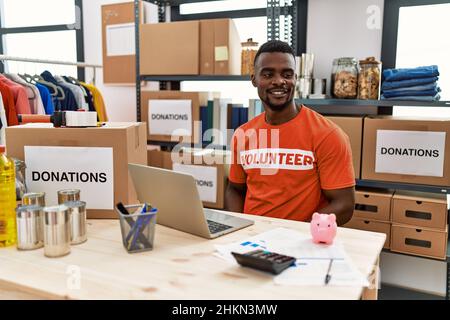 Young african man working as volunteer t shirt at donations stand looking away to side with smile on face, natural expression. laughing confident. Stock Photo