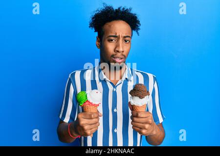 Young african american man with beard holding two ice cream cones clueless and confused expression. doubt concept. Stock Photo