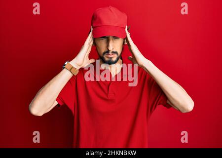 Young hispanic man wearing delivery uniform and cap suffering from headache desperate and stressed because pain and migraine. hands on head. Stock Photo