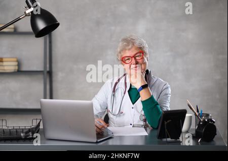 Middle age female doctor using laptop, writing notes with stethoscope on table. Healthcare concept. Medical doctor writing and taking notes Stock Photo