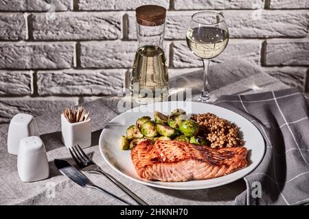 grilled salmon fillet with roast brussel sprouts and cooked farro on a plate with restaurant table setting, white wine in glass and in decanter, vinta Stock Photo