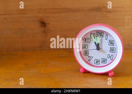 A round clock stands on a wooden shelf. An object with a pink case and a white dial Stock Photo