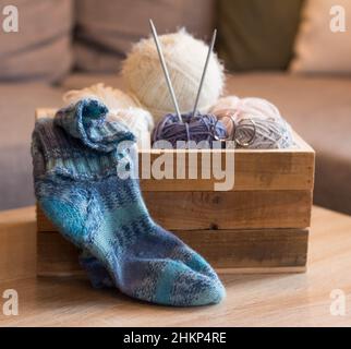 knitted blue socks with woolen balls in a wooden box and knitting needles handmade Stock Photo