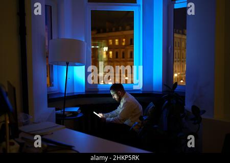 Exhausted young businessman texting family about staying at work overtime. Overwork and tiredness Stock Photo