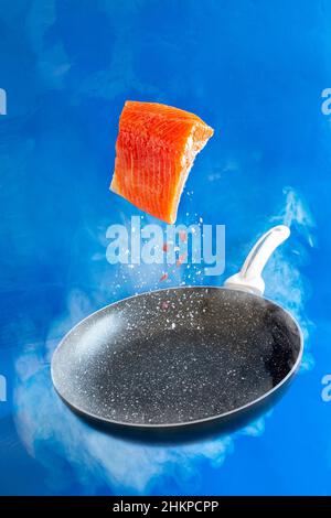 Close-up photo of fresh raw salmon, trout fillet floating in the air above the frying pan on the blue water background Stock Photo