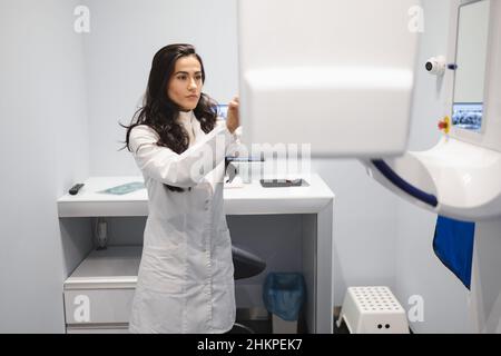 Woman in a medical coat adjusts a dental tomograph. Medical worker in the X-ray room Stock Photo