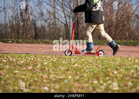 Boy riding scooter near lake. Child with red sports equipment. Stock Photo