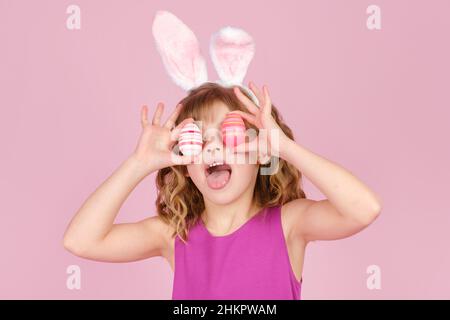 Little girl in Easter bunny ears smiling while covering eyes with colorful eggs  Stock Photo