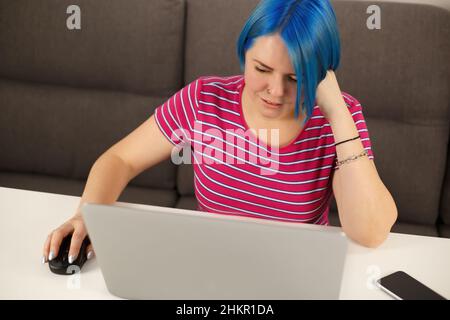 Young white woman with blue hair working on laptop computer. Cute Caucasian female with colored bob hairstyle using modern notebook pc for online work