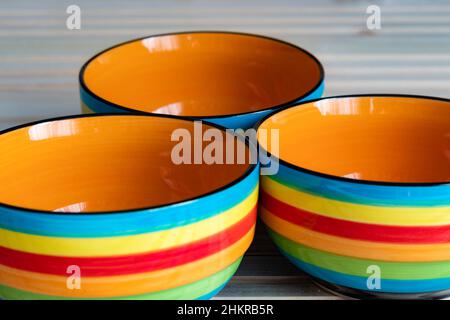 Close-up photo of three striped bowls, colored in red, blue, yellow, orange and green, on a wooden background Stock Photo