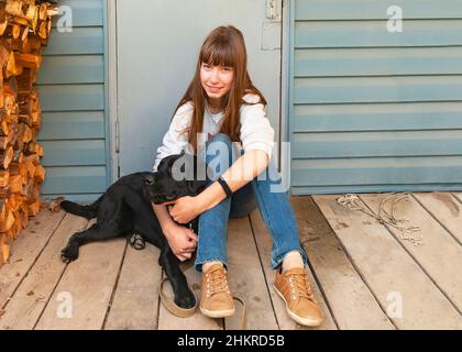 A teenage girl sits with a black labrador on the porch of the bathhouse Stock Photo